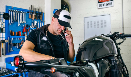 Mechanic talking phone while fixing motorbike