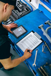 Mechanic using tablet app and taking notes