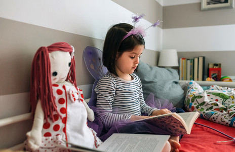 Girl disguised as a butterfly reading with her doll