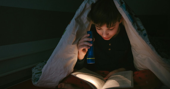 Boy reading with a flashlight