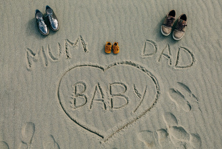 Mum dad and baby written on the sand of the beach