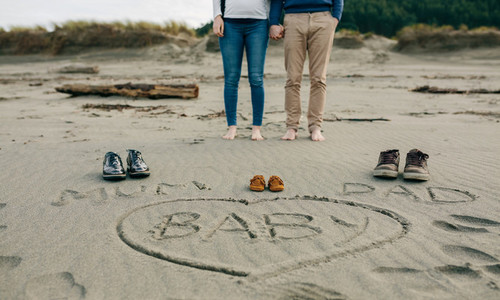 Mum  dad and baby written on the sand with the parents behind
