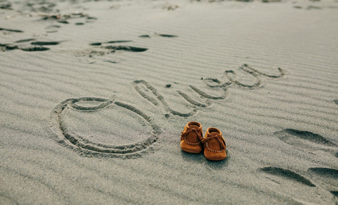 Baby name written in sand with shoes