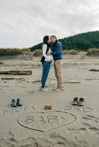 Mum  dad and baby written on the sand with the parents kissing behind