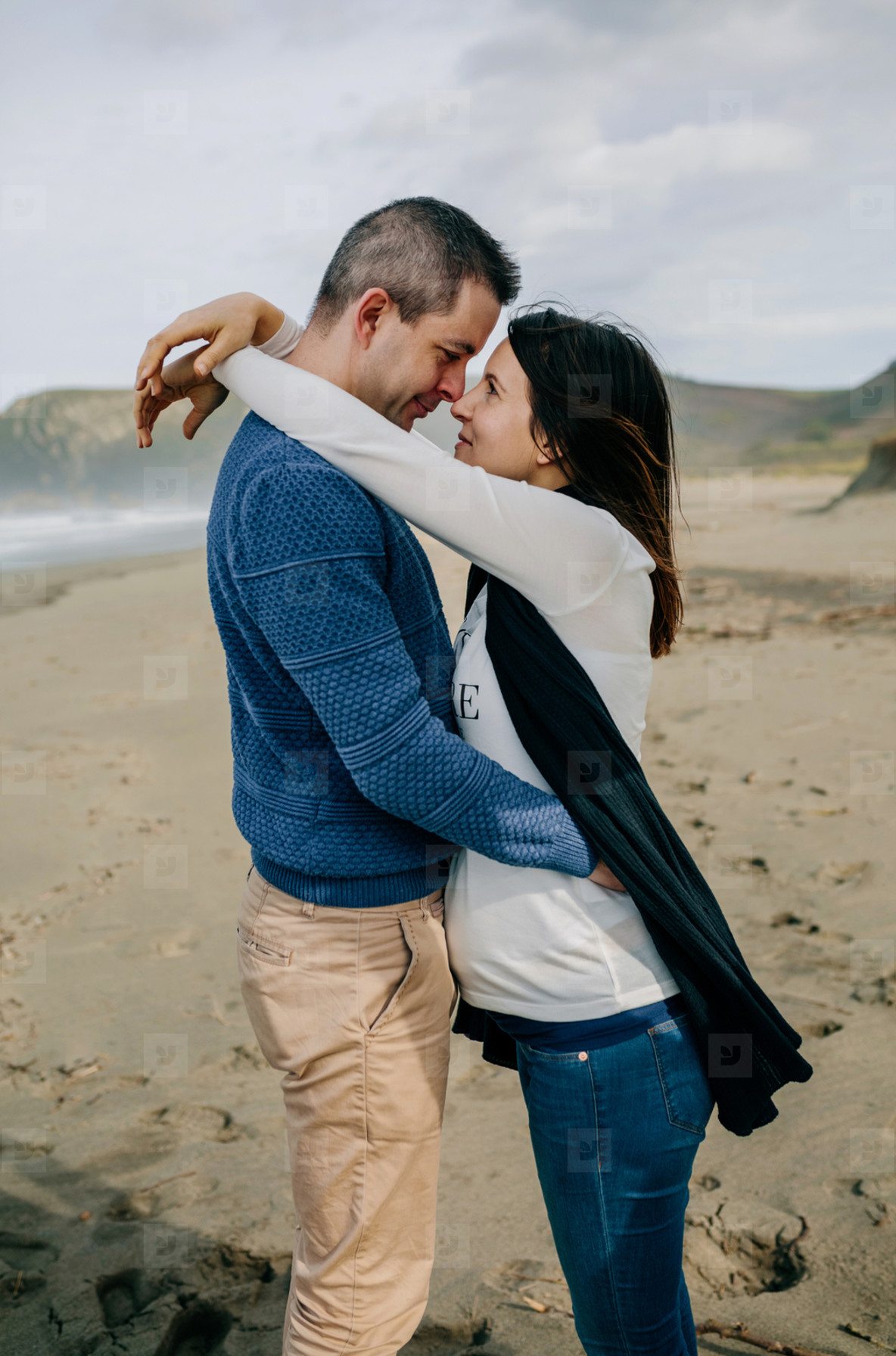 Pregnant woman hugging partner on the beach