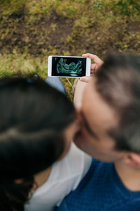 Pregnant looking ultrasound on the mobile with her husband and kissing