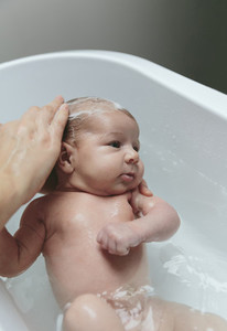 Newborn in the bathtub with her mother washing her hair