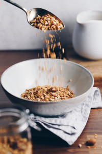 Hand sprinkles baked granola in a ceramic bowl  Healthy vegetarian breakfast