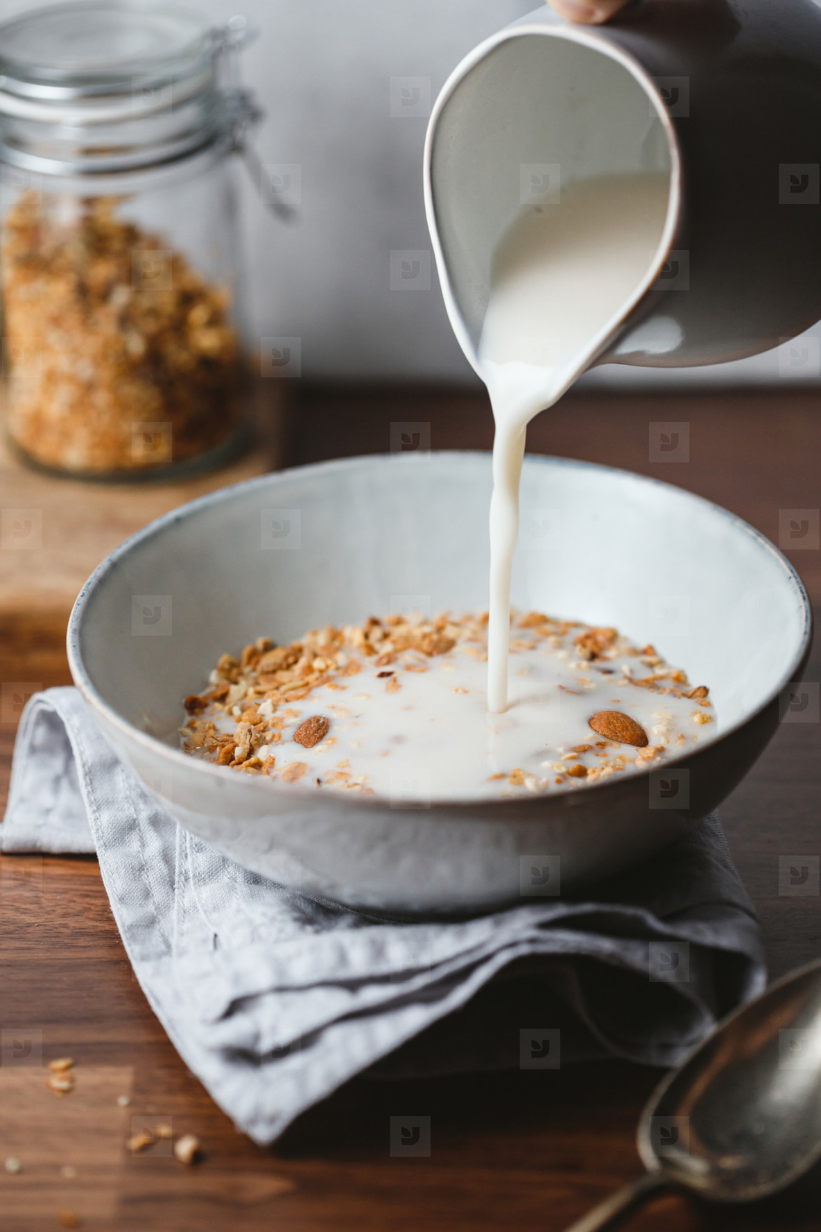 Almond milk is poured in a ceramic bowl with baked granola  Healthy vegetarian breakfast