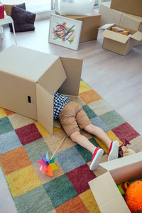 Boy playing inside a moving box while his father unpacks