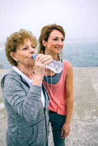 Senior sportswoman drinking water with female coach