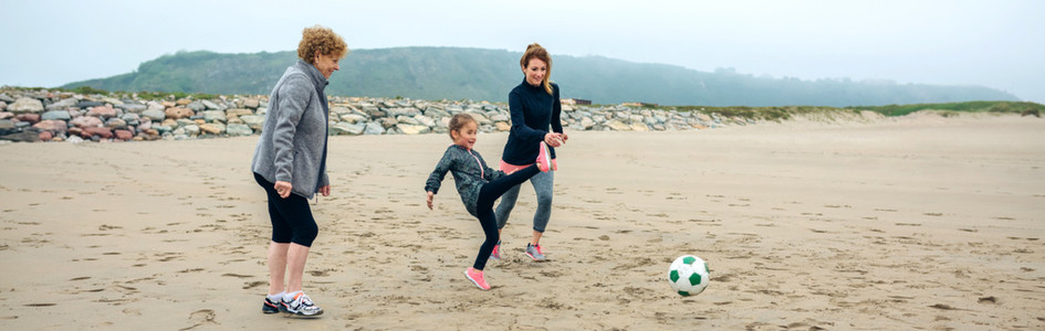 Three generations female playing soccer on the beach