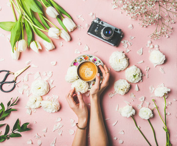 Female hands holding cup of coffee  flowers and film camera