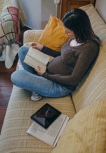 Pregnant reading a book on the couch