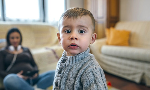 Little boy looking at camera with his pregnant mother sitting in background