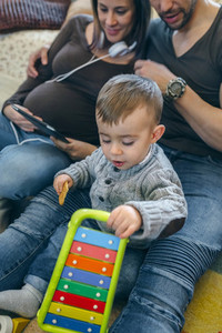 Pregnant woman and husband looking tablet while son plays