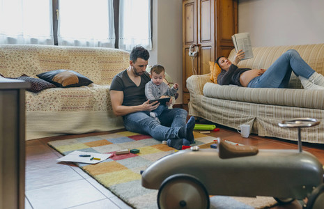Father looking tablet with little son while the pregnant mother reads a magazine