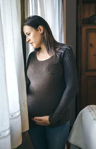 Pregnant woman caressing belly and looking window