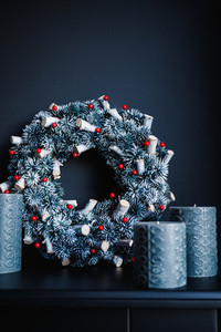 Grey candles and Christmas wreath on a decorative fireplace against black wall  Holidays decorations in a dark monochrome room interior