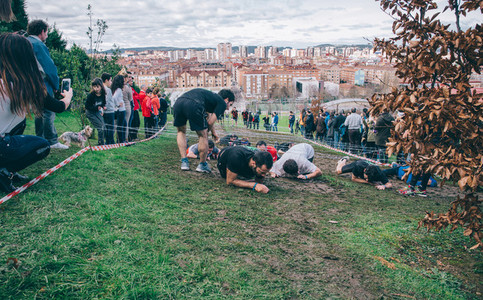 Runners crawling under barbed wire in a test of extreme obstacle race