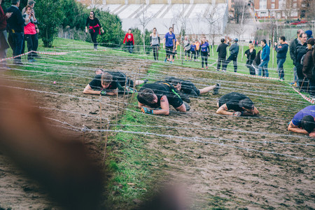 Runners crawling under barbed wire in a test of extreme obstacle race