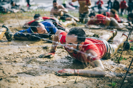 Runner crawling under barbed wire in a test of extreme obstacle race