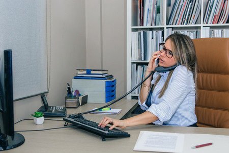 Busy businesswoman talking with cell and fixed line phone in office