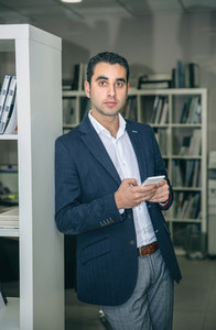Businessman holding smartphone leaning on a bookcase