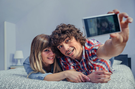 Couple in love taking selfie with smartphone on bed