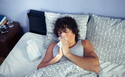 Sick man sneezing and covering nose with tissue