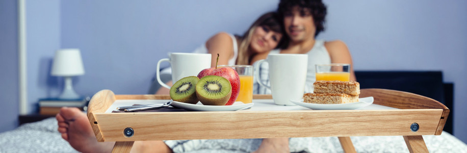 Healthy breakfast on tray and couple lying in background