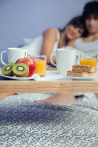 Healthy breakfast on tray and couple lying in background