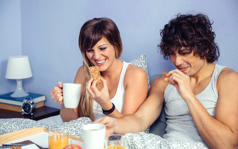 Couple laughing and having breakfast in bed at home