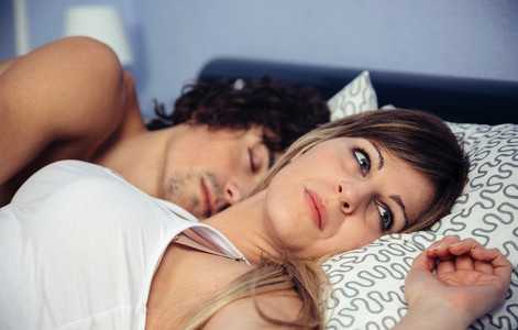 Thoughtful woman lying near her sleeping boyfriend