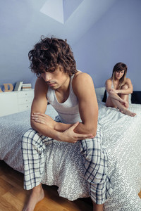 Angry man sitting over bed with woman on background