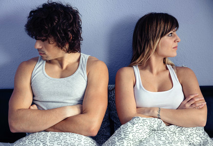 Angry couple sitting on bed with crossed hands