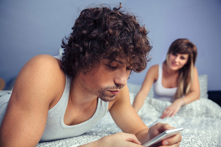 Man lying using smartphone and woman sitting on bed