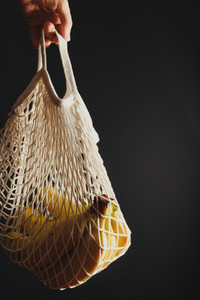 Hand holds an eco net bag with banana branch against black background