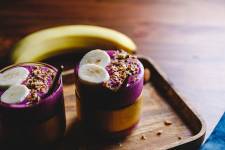 Two glasses with violet berry and banana smoothie are served crushed almond on a wooden tray
