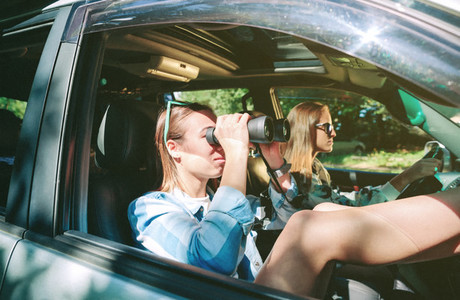 Woman looking through the binoculars and friend driving