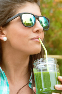 Woman with sunglasses drinking green vegetable smoothie outdoors