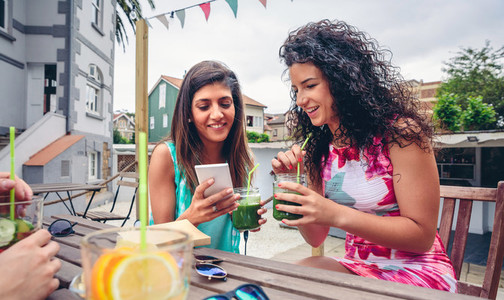 Two women looking smartphone and drinking green smoothies