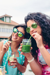 Two women with sunglasses drinking organic beverages outdoors