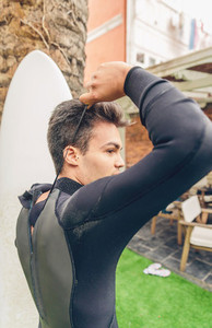 Young surfer man with surfboard closing wetsuit