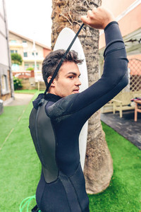 Young surfer man with surfboard closing wetsuit