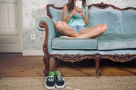 Woman looking smartphone sitting on sofa with legs crossed