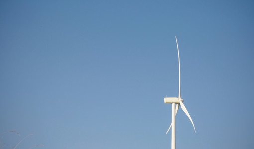 Wind turbine generating electricity over blue sky background