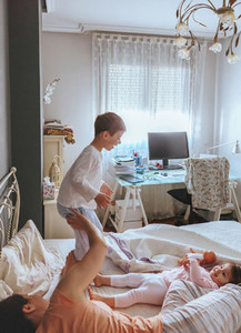 Boy jumping over the bed with his family