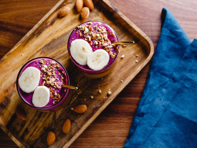 Top view of two glasses with violet berry and banana smoothie are served crushed almond on a wooden tray