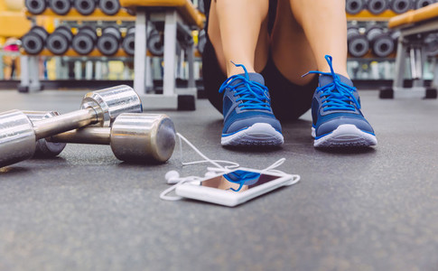 Sporty man sitting with dumbbells and smartphone in gym floor